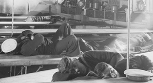 Detail from a glass plate negative of naval ratings asleep at mess tables on HMS Inflexible, presumably during her trials, 1908. The original negative is cracked (UCS1/118/374/39).